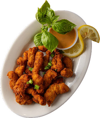 A white plate with pieces of fried chicken, garnished with lemon slices, green herbs, and fresh basil leaves.