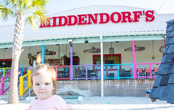 A young child stands in front of a colorful seaside restaurant named 