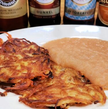 A plate with several potato pancakes next to a serving of applesauce, with assorted beer bottles in the background.