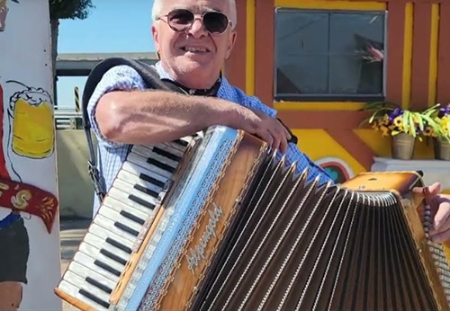 A person plays a large accordion in front of a colorful backdrop, enjoying a lively outdoor atmosphere.