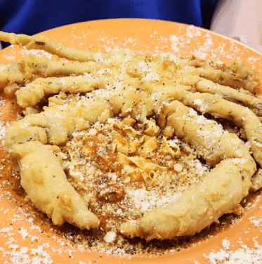 A whole fried soft-shell crab served on a bed of creamy mashed potatoes, topped with grated cheese and black pepper on an orange plate.